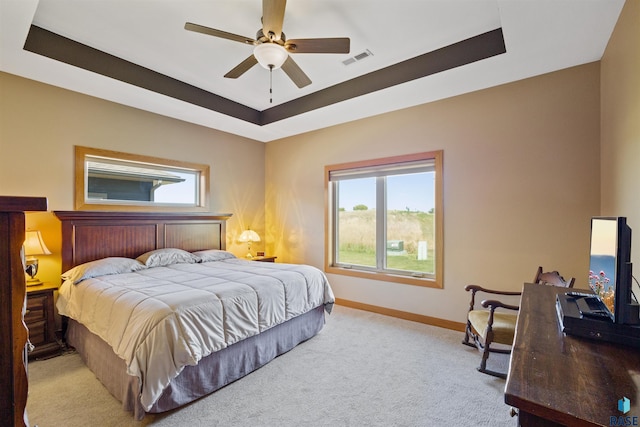 carpeted bedroom with a raised ceiling and ceiling fan