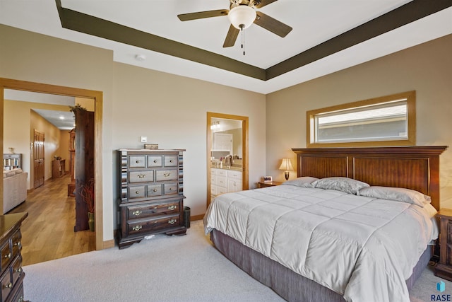 carpeted bedroom with ceiling fan, ensuite bathroom, and a tray ceiling