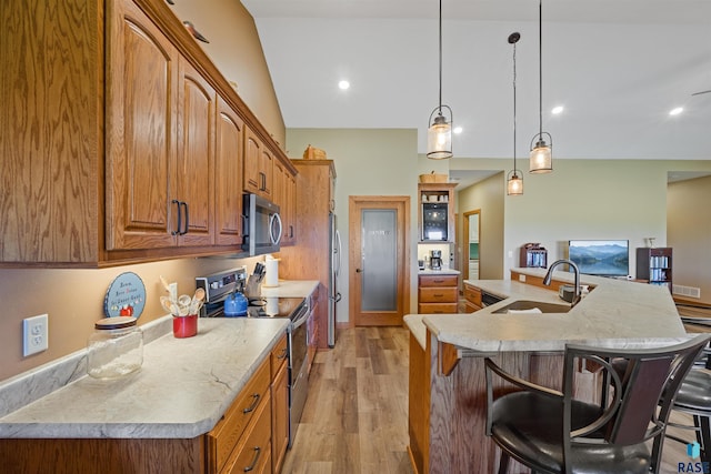 kitchen featuring a large island, appliances with stainless steel finishes, decorative light fixtures, light wood-type flooring, and sink