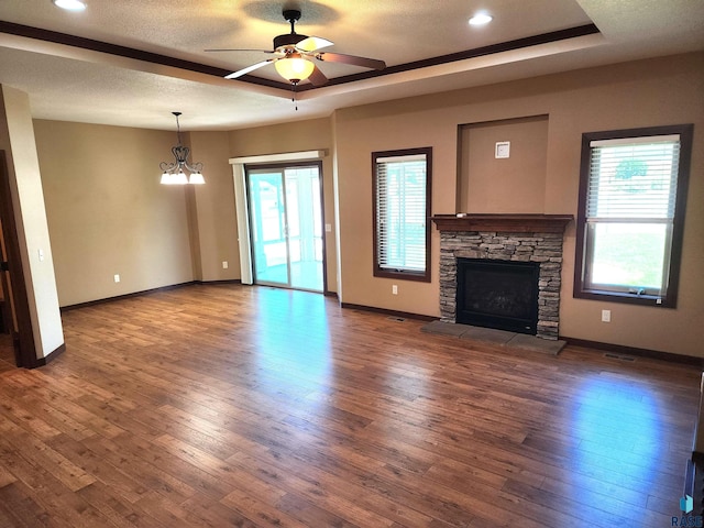 unfurnished living room with a raised ceiling, dark hardwood / wood-style flooring, a wealth of natural light, and a stone fireplace