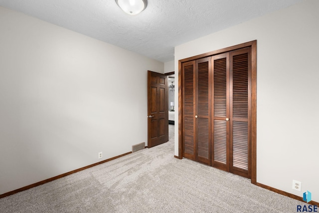 unfurnished bedroom featuring a textured ceiling, carpet flooring, visible vents, baseboards, and a closet