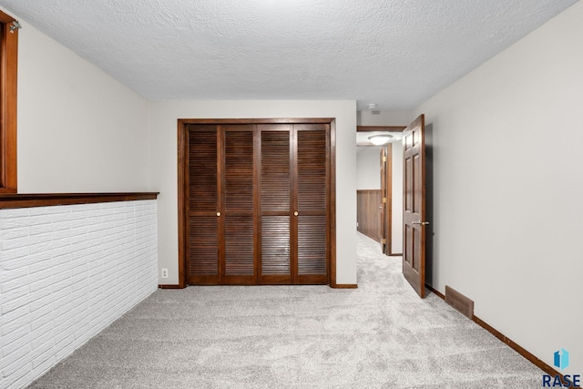 unfurnished bedroom with a textured ceiling, a closet, baseboards, and light colored carpet