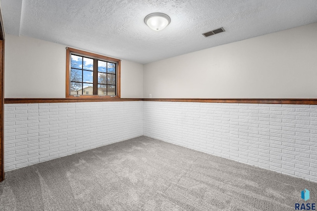 carpeted spare room featuring a wainscoted wall, brick wall, visible vents, and a textured ceiling