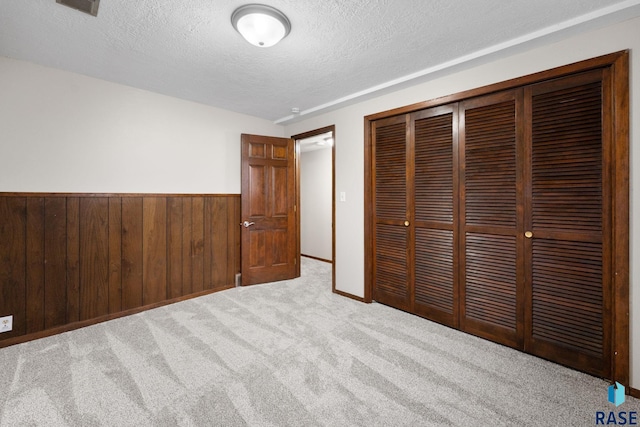 unfurnished bedroom with wooden walls, wainscoting, a textured ceiling, carpet flooring, and a closet