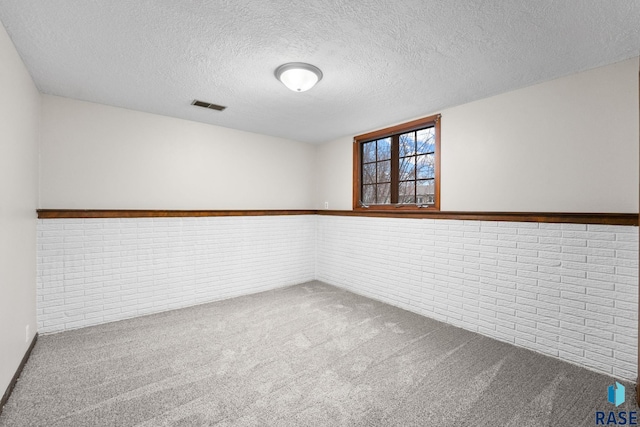 spare room with a wainscoted wall, visible vents, carpet flooring, a textured ceiling, and brick wall