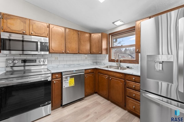 kitchen featuring appliances with stainless steel finishes, decorative backsplash, sink, light hardwood / wood-style floors, and vaulted ceiling