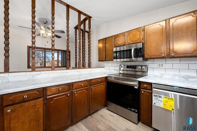 kitchen with light wood finished floors, stainless steel appliances, tasteful backsplash, brown cabinetry, and ceiling fan