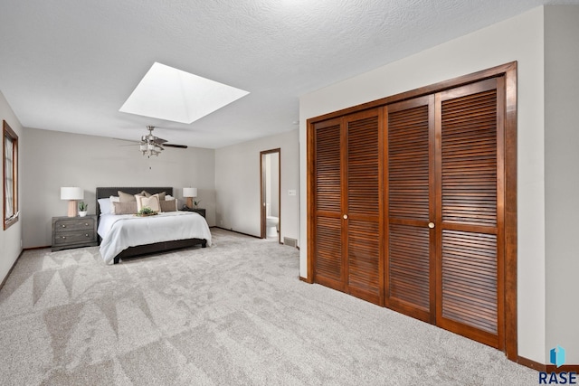 carpeted bedroom featuring a skylight, a closet, ceiling fan, a textured ceiling, and baseboards