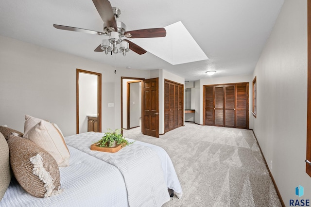 bedroom with light carpet, ceiling fan, a skylight, and two closets