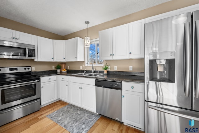 kitchen with light hardwood / wood-style floors, stainless steel appliances, hanging light fixtures, white cabinets, and sink