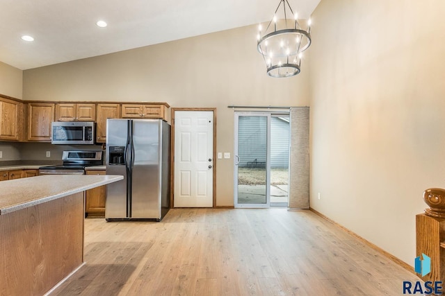 kitchen featuring appliances with stainless steel finishes, light wood-type flooring, high vaulted ceiling, a chandelier, and pendant lighting