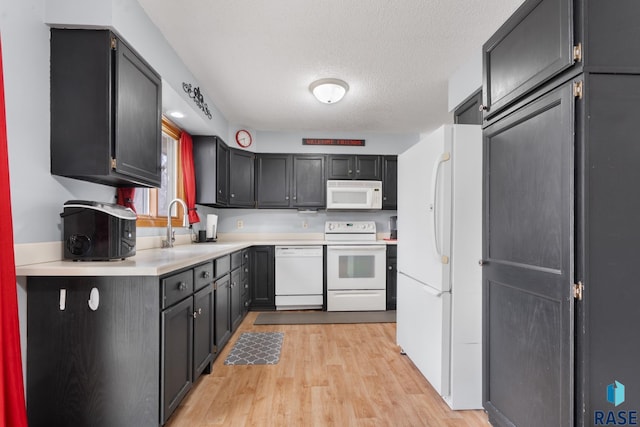 kitchen with sink, white appliances, a textured ceiling, and light wood-type flooring