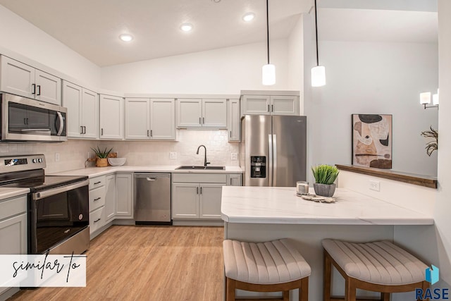 kitchen featuring appliances with stainless steel finishes, a kitchen breakfast bar, vaulted ceiling, pendant lighting, and sink