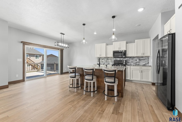 kitchen featuring black refrigerator, an island with sink, decorative light fixtures, stove, and white cabinets