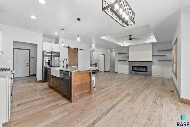 kitchen with a barn door, an island with sink, appliances with stainless steel finishes, a tray ceiling, and decorative light fixtures