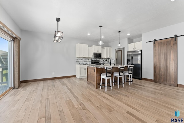 kitchen with decorative light fixtures, a barn door, a kitchen island with sink, white cabinets, and stainless steel fridge