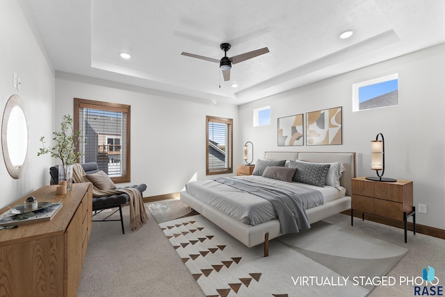 carpeted bedroom with ceiling fan and a tray ceiling