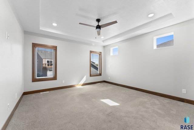 carpeted spare room with ceiling fan and a raised ceiling