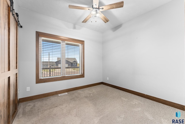 empty room with ceiling fan, a barn door, and carpet flooring