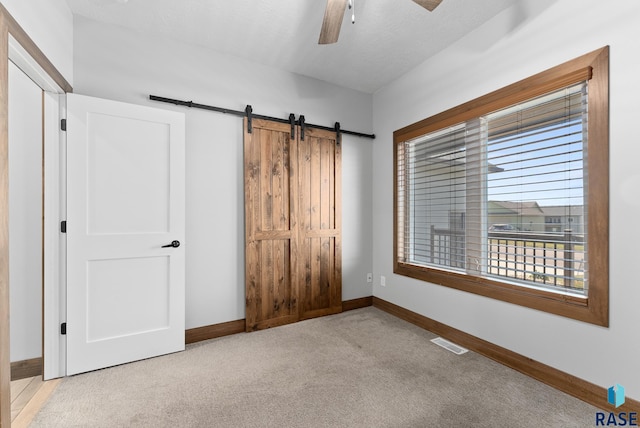 unfurnished bedroom featuring ceiling fan, light colored carpet, and a barn door