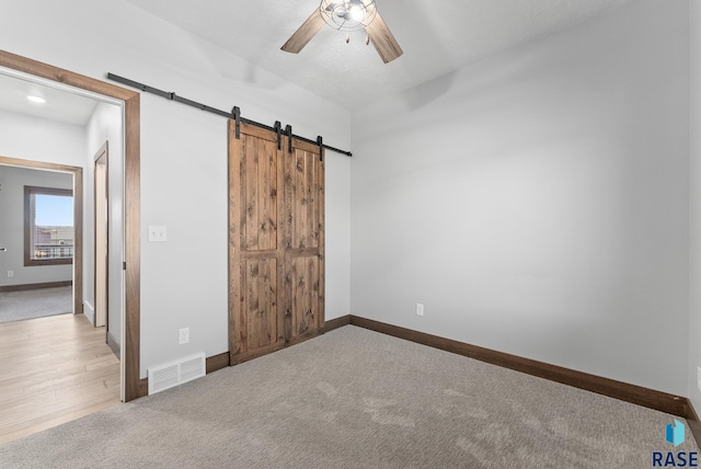 unfurnished bedroom with ceiling fan, a barn door, and light colored carpet