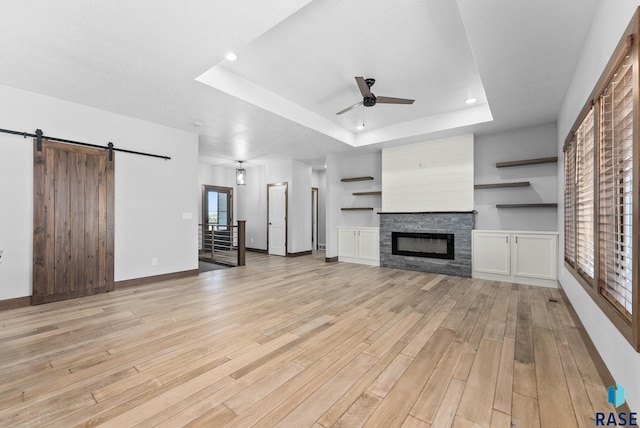 unfurnished living room featuring ceiling fan, light hardwood / wood-style flooring, a raised ceiling, and a barn door