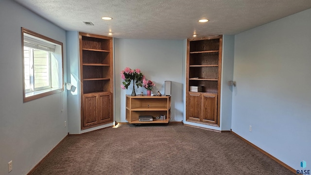 empty room with built in features, dark carpet, and a textured ceiling