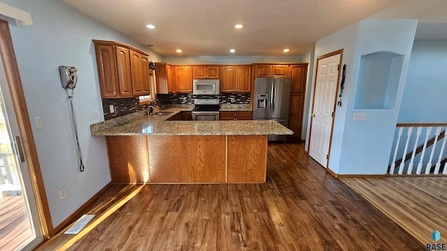 kitchen featuring appliances with stainless steel finishes, kitchen peninsula, light stone counters, and sink