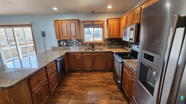 kitchen featuring kitchen peninsula, stainless steel appliances, backsplash, light stone countertops, and sink