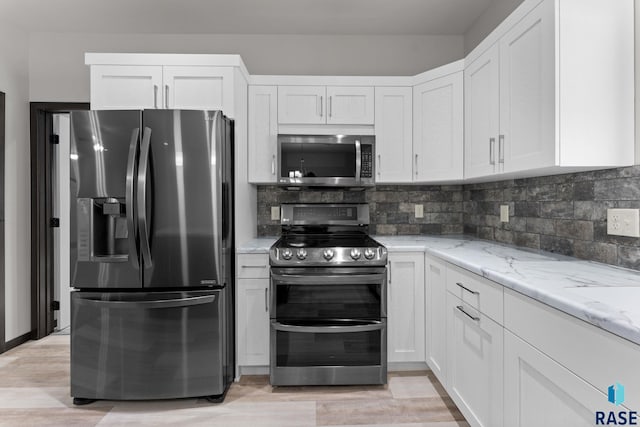 kitchen with light stone countertops, white cabinets, stainless steel appliances, backsplash, and light wood-type flooring