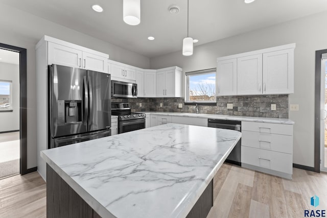 kitchen with white cabinets, appliances with stainless steel finishes, a kitchen island, decorative backsplash, and hanging light fixtures