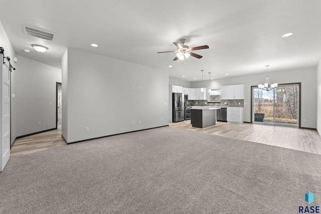 unfurnished living room featuring ceiling fan with notable chandelier, light carpet, and a barn door