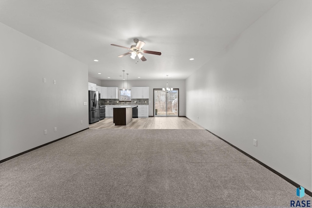 unfurnished living room featuring light carpet and ceiling fan with notable chandelier