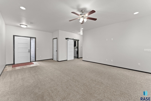 carpeted spare room with ceiling fan and a barn door