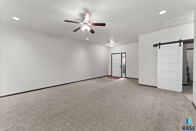 carpeted spare room featuring ceiling fan and a barn door