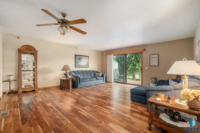 living room featuring ceiling fan, light wood-type flooring, and a textured ceiling