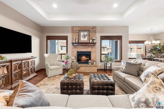 living room featuring an inviting chandelier, a fireplace, hardwood / wood-style flooring, and a tray ceiling