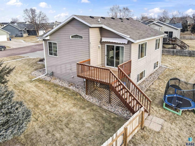 back of house with a trampoline, a yard, and a wooden deck