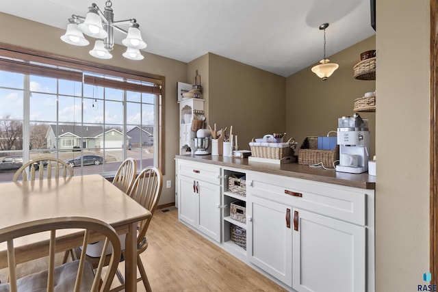 kitchen with light wood-type flooring, an inviting chandelier, white cabinets, and decorative light fixtures