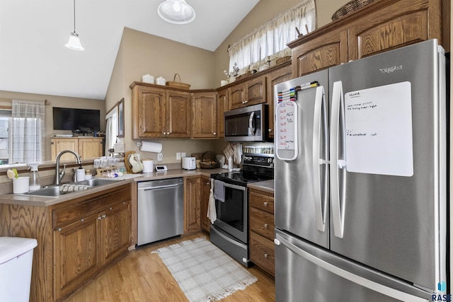 kitchen featuring pendant lighting, appliances with stainless steel finishes, lofted ceiling, sink, and light hardwood / wood-style flooring