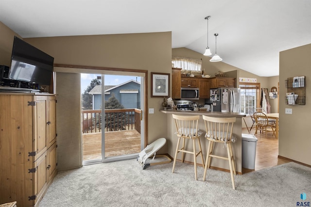 kitchen featuring pendant lighting, appliances with stainless steel finishes, lofted ceiling, kitchen peninsula, and a breakfast bar area