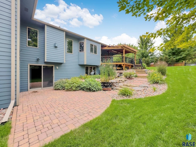 rear view of house with a lawn, a wooden deck, and a patio