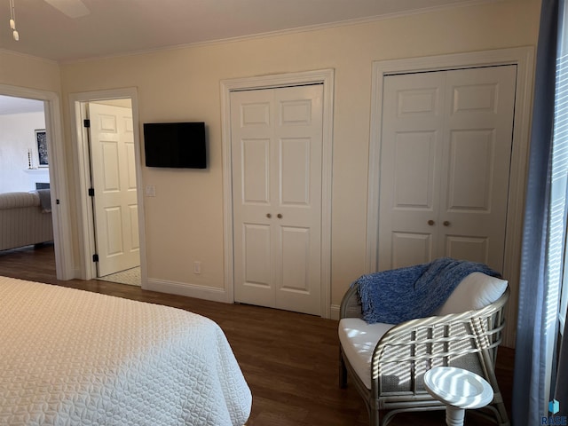 bedroom with ceiling fan, dark hardwood / wood-style flooring, two closets, and ornamental molding