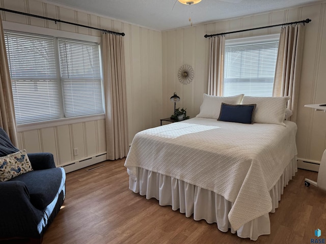 bedroom with ceiling fan, a baseboard heating unit, a textured ceiling, and light hardwood / wood-style floors