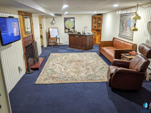 carpeted living room featuring a brick fireplace and wooden walls