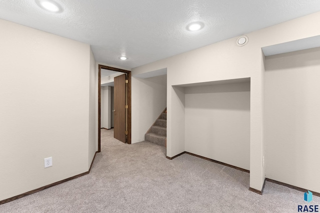 basement featuring light colored carpet and a textured ceiling