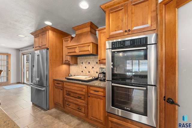 kitchen with custom exhaust hood, backsplash, light stone countertops, light tile patterned flooring, and stainless steel appliances