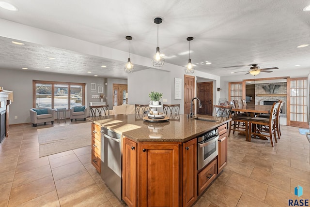 kitchen with appliances with stainless steel finishes, a fireplace, sink, decorative light fixtures, and an island with sink