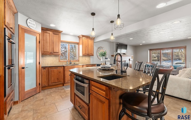 kitchen with sink, a kitchen island with sink, decorative backsplash, and dark stone counters