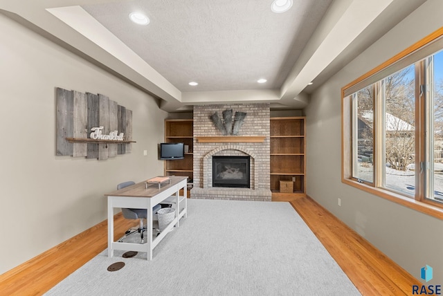 living room with a raised ceiling, a brick fireplace, light hardwood / wood-style floors, and a textured ceiling